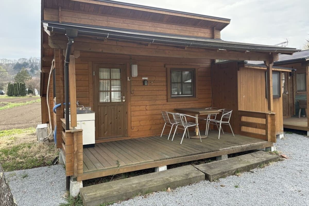 A wooden cabin with a deck, a small table with chairs, and a window.