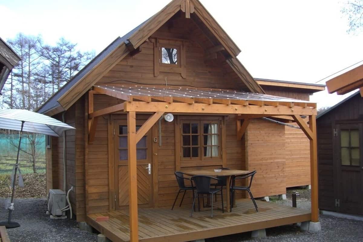 A wooden cabin with a porch, a table, and chairs.