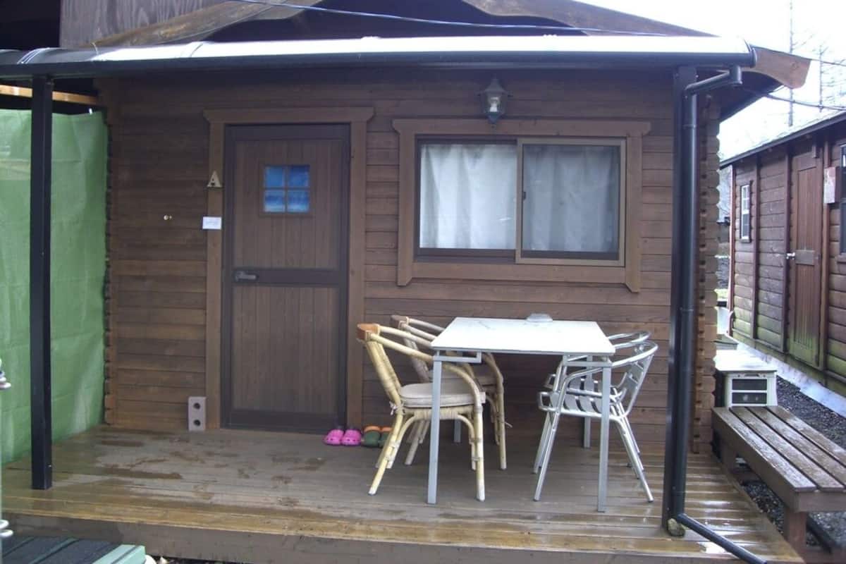 A wooden cabin with a covered porch, a table, and chairs.