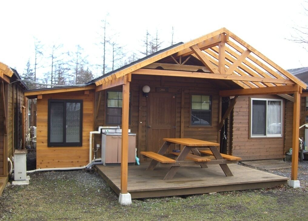 Eine Holzhütte mit überdachter Veranda, einem Picknicktisch und einer kleinen Küchenzeile.