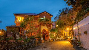 A two-story building with a brick facade, a central archway, and a small garden area with potted plants. - Villa Katsuyama Avail (Kyonan)