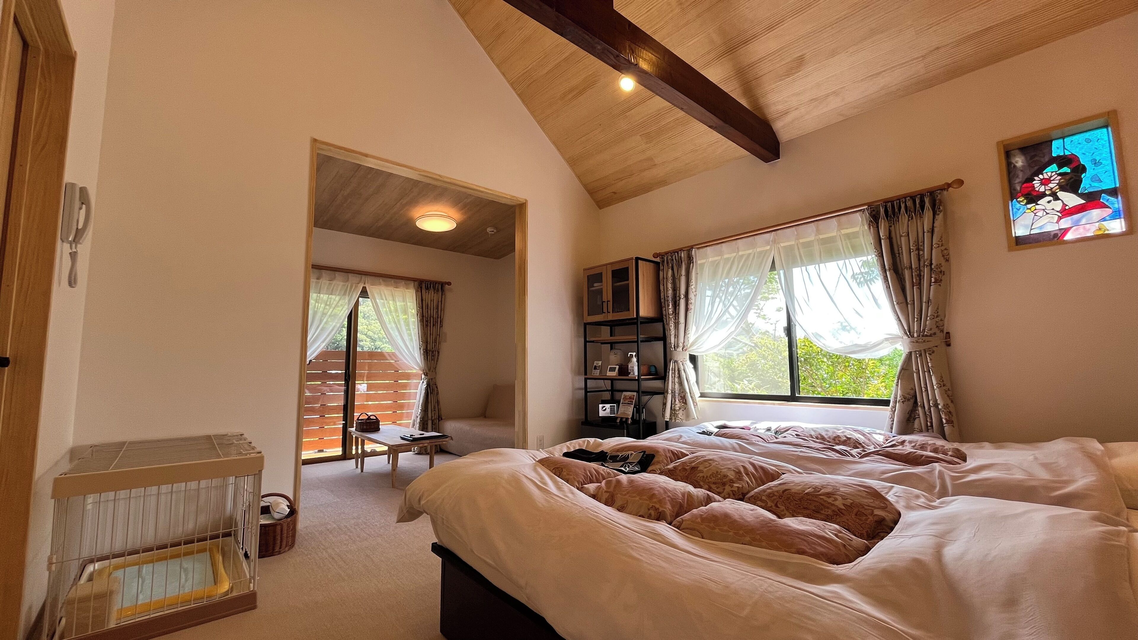 Ein Schlafzimmer mit einem großen Bett, Holzboden, einem kleinen Tisch und einem Fenster mit Vorhängen.