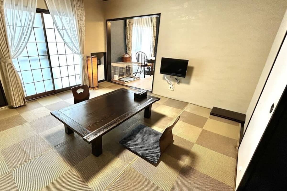 A traditional Japanese-style room with tatami flooring, a low table, a television, and a sliding door leading to an adjacent space.