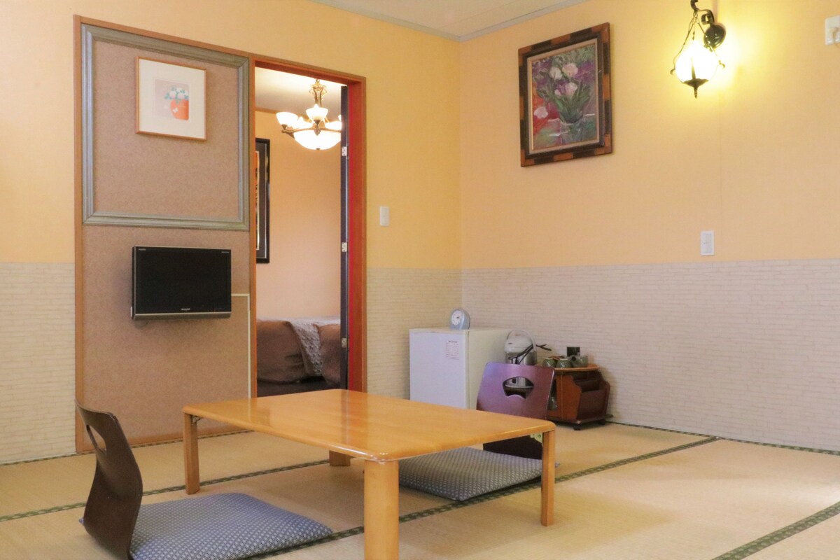 A traditional Japanese-style room with tatami flooring, a low wooden table, a television, and a small refrigerator.