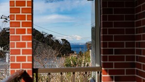 A view through a window with a brick wall, a clear sky, and a distant view of a coastal area with a mountain. - Villa Katsuyama Avail (Kyonan)
