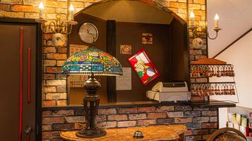 A hotel lobby with a brick wall, a clock, a stained glass lamp, a cash register, and a key display.