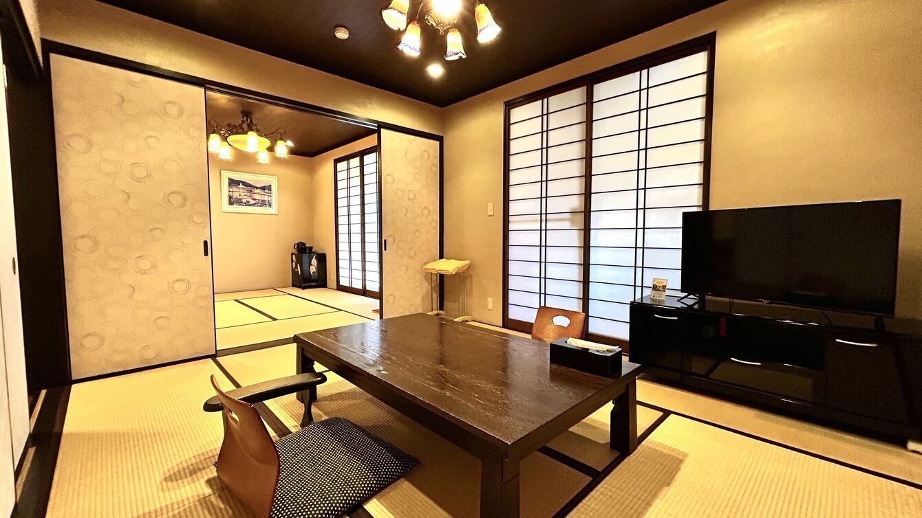 Ein traditioneller japanischer Raum mit Tatami-Böden, einem niedrigen Tisch, einem Fernseher und Schiebetüren.