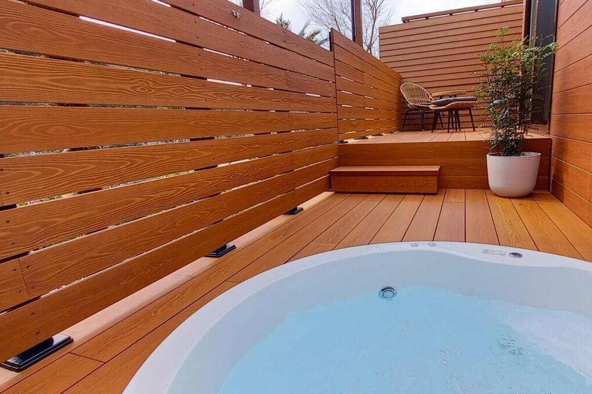 A wooden deck with a hot tub, a potted plant, and a seating area.