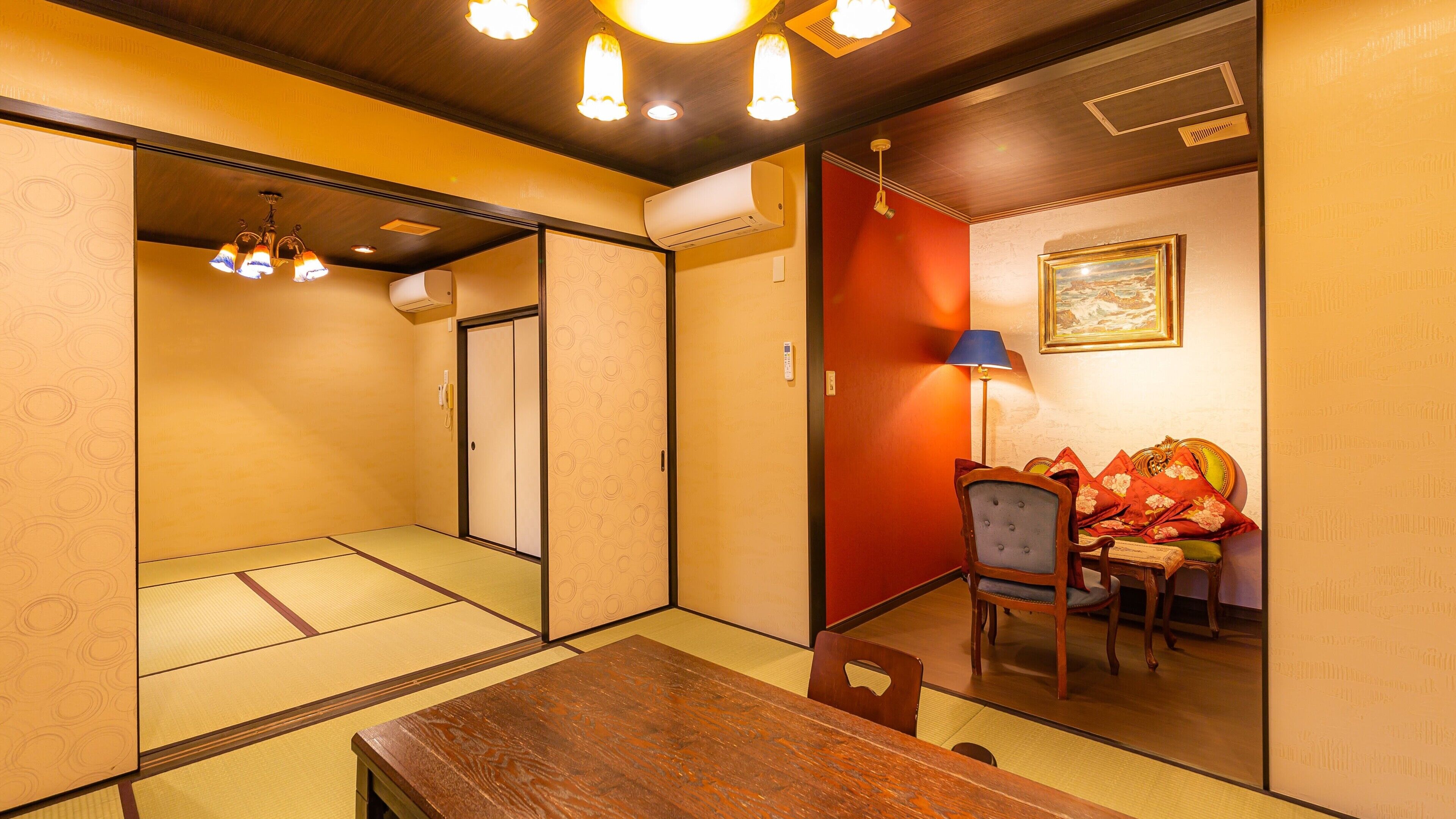Ein traditioneller japanischer Raum mit Tatami-Böden, einem Holztisch, einem Stuhl, einem Schreibtisch mit Lampe und einem Bild an der Wand.