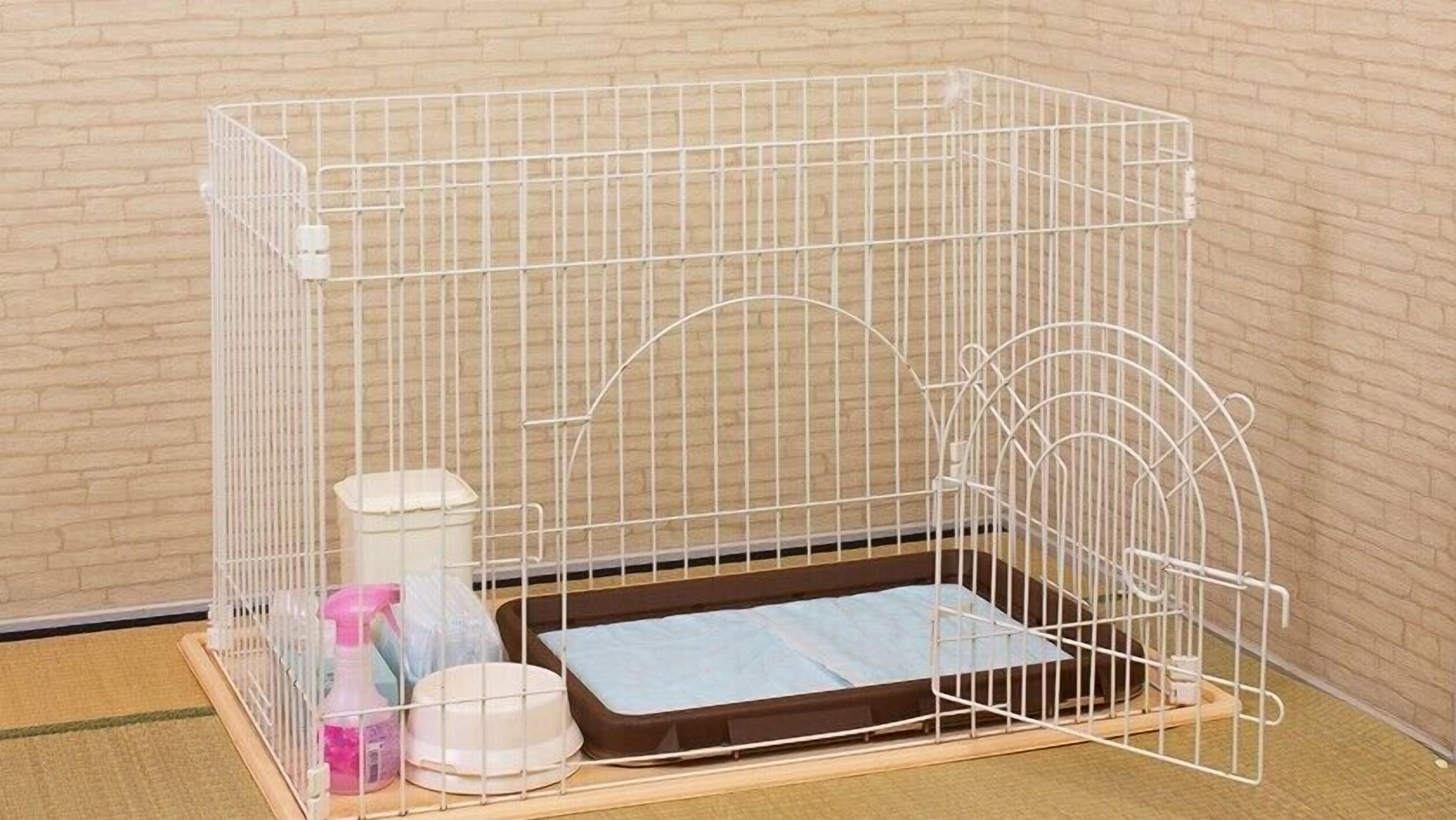 Une cage en métal blanc avec un tapis bleu, un récipient blanc et un flacon pulvérisateur.