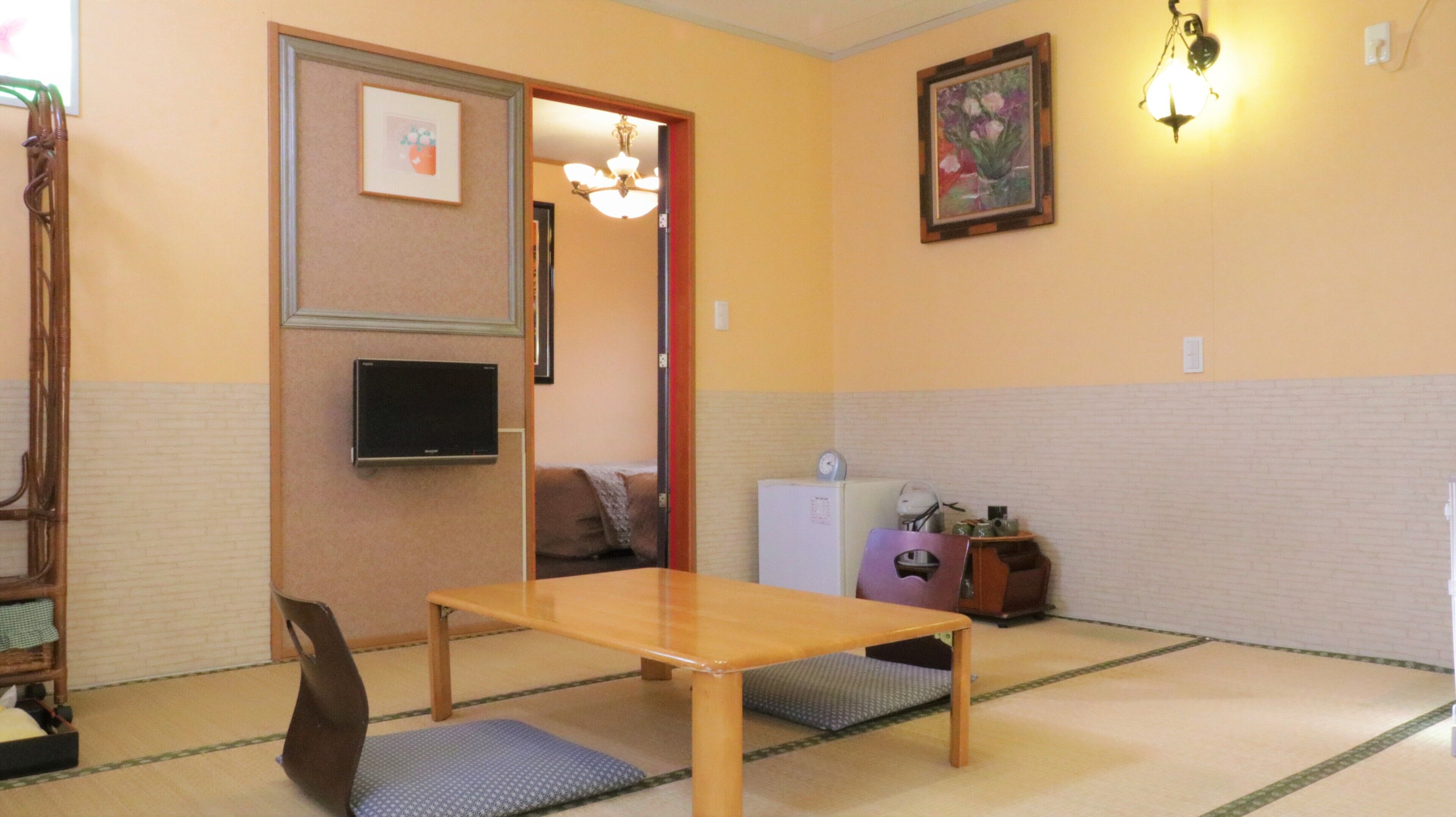 Ein traditionell eingerichteter japanischer Raum mit Tatami-Böden, einem niedrigen Holztisch, einem Fernseher und einem kleinen Kühlschrank.