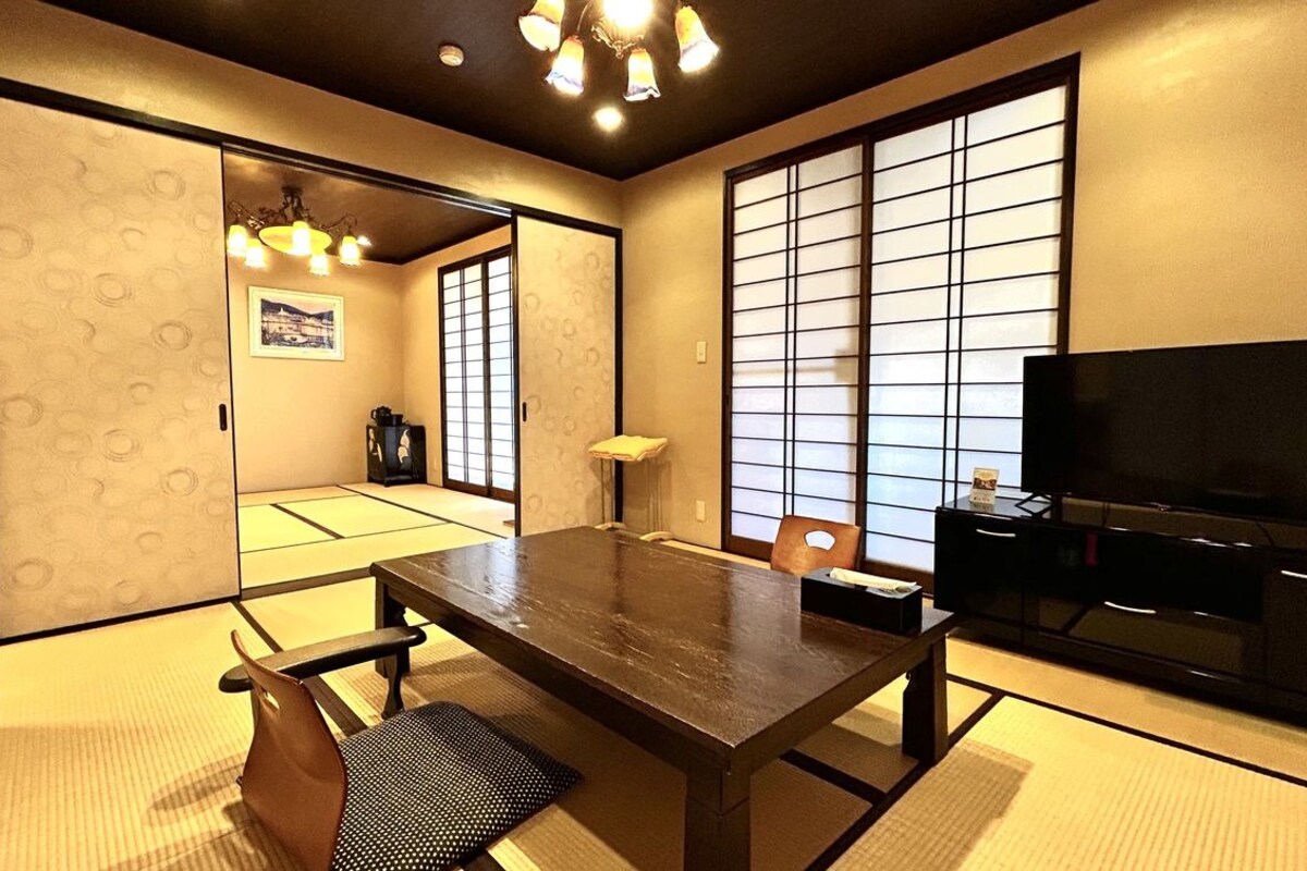 A traditional Japanese-style room with tatami flooring, a low table, a television, and sliding doors.