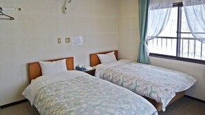 Une chambre d’hôtel avec deux lits, une fenêtre avec des rideaux légers, une lampe fixée au mur et une petite table avec un téléphone.