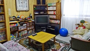 Une pièce avec une télévision, des étagères à livres, une petite table, un ours en peluche et un ballon d’exercice bleu.