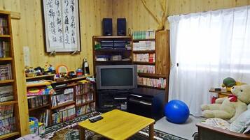 Une pièce avec une télévision, des étagères à livres, une petite table, un ours en peluche et un ballon d’exercice bleu.