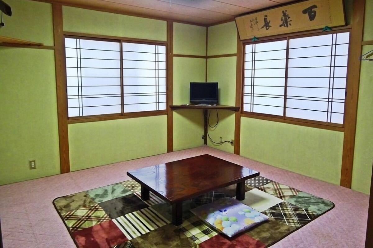 Una habitación japonesa tradicional con suelo de tatami, una mesa de madera baja y un televisor sobre una estantería.