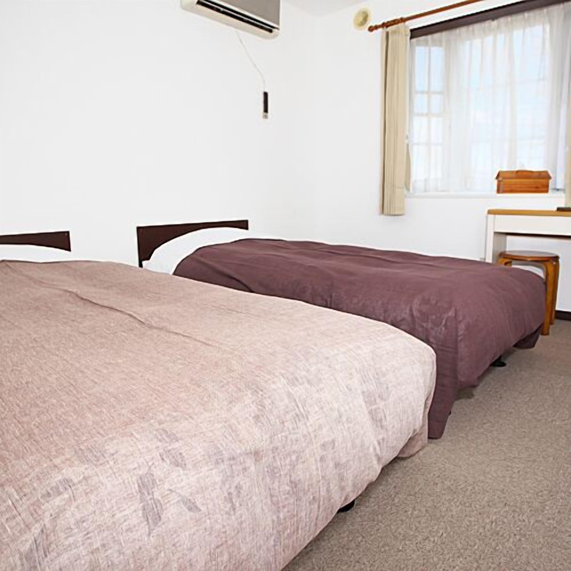 A room with two beds, a desk, and an air conditioning unit.