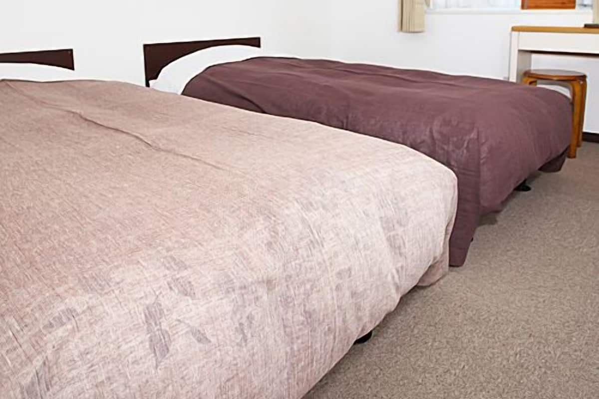 A room with two beds, a desk, and an air conditioning unit.