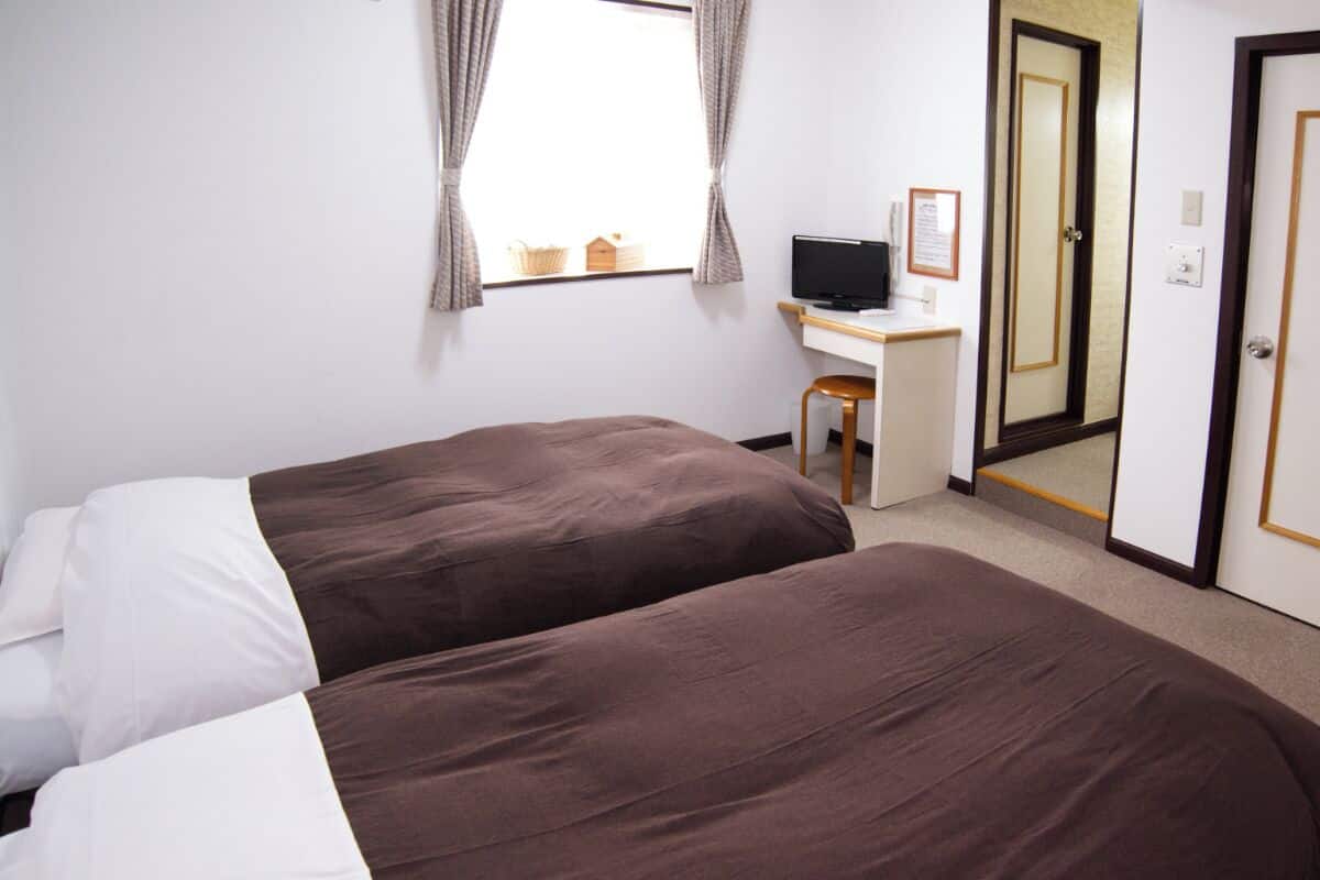 A hotel room with two beds, a desk, a television, and a mirror.