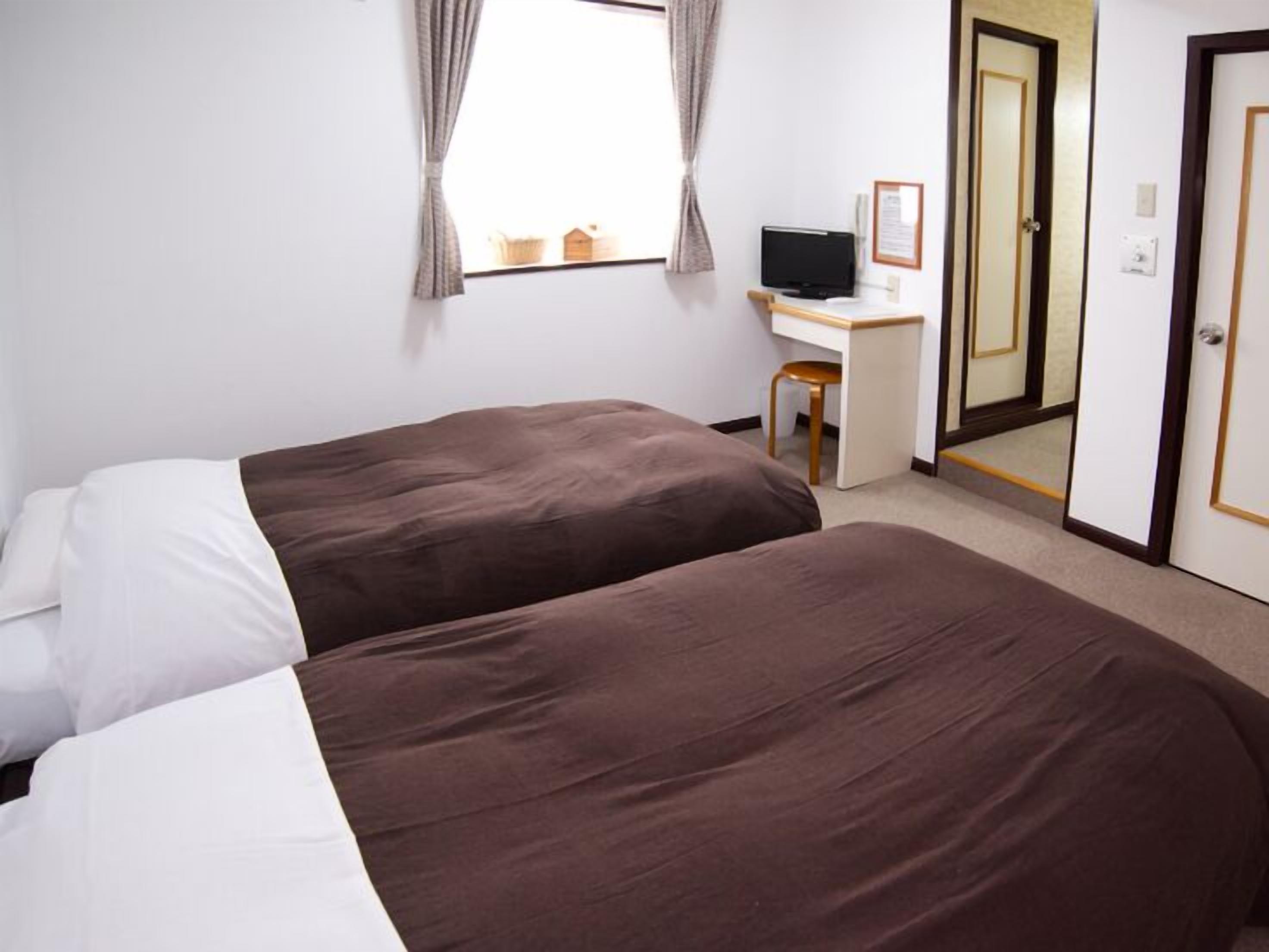 A hotel room with two beds, a desk, a chair, a television, and a door.