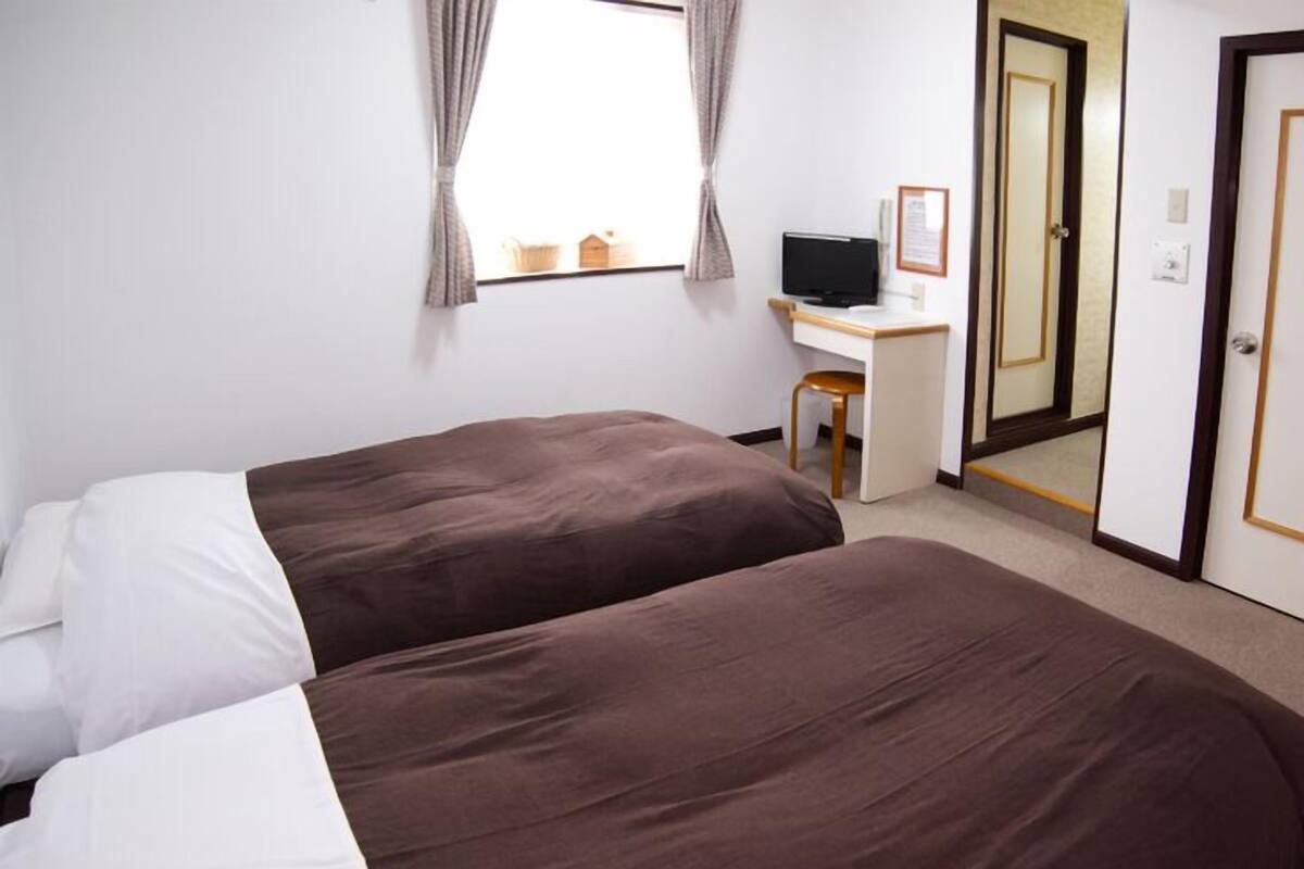 A hotel room with two beds, a desk, a chair, a television, and a door.