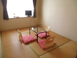 Una habitación con tatami, una mesa baja, dos sillas y un televisor sobre un mueble.