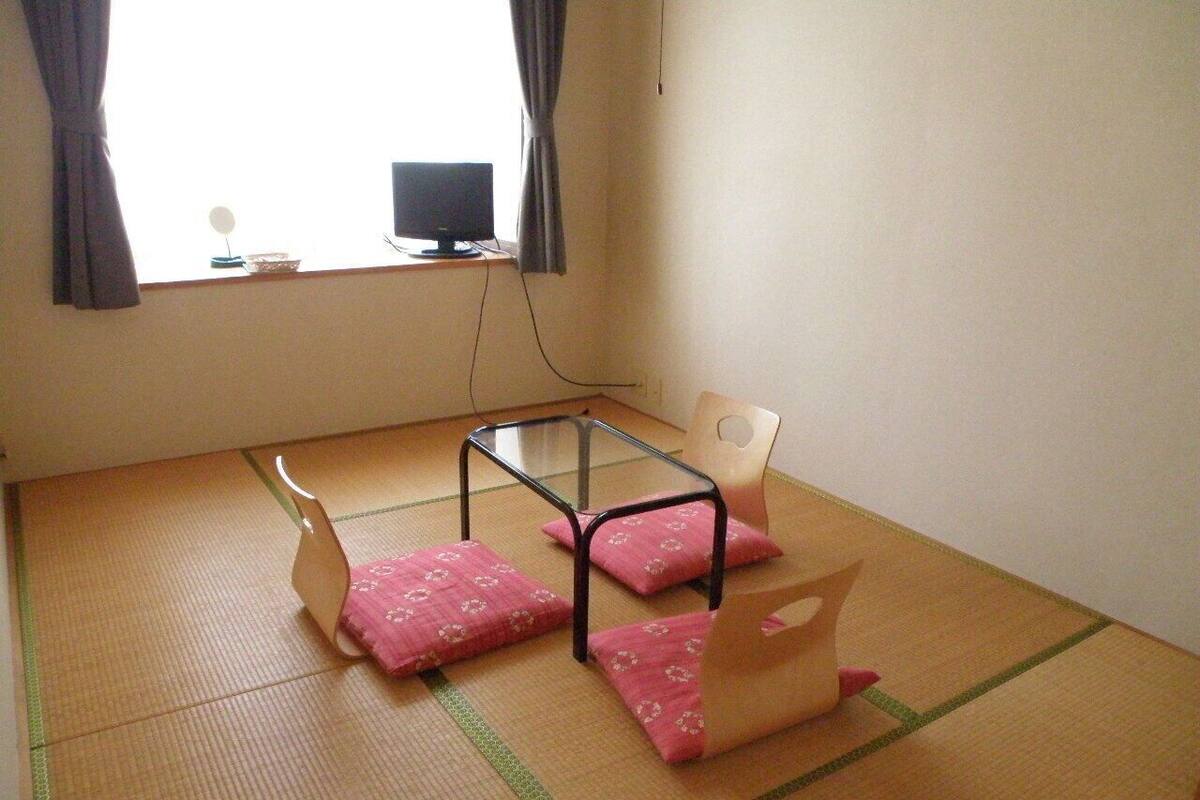 Une pièce avec un sol recouvert de tatamis, une petite table basse, deux chaises et un téléviseur posé sur un meuble.