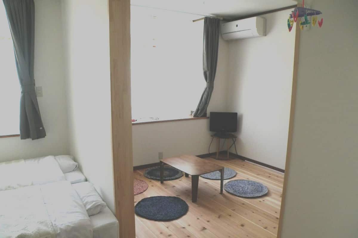 Une chambre avec un lit, une petite table, une télévision et une fenêtre avec des rideaux.