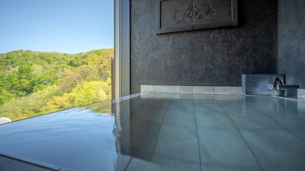 A modern bathroom with a glass-enclosed shower, a dark textured wall, and a framed decorative piece. - Aone Onsen Itto Onsenyado Seigetsu (Kawasaki)