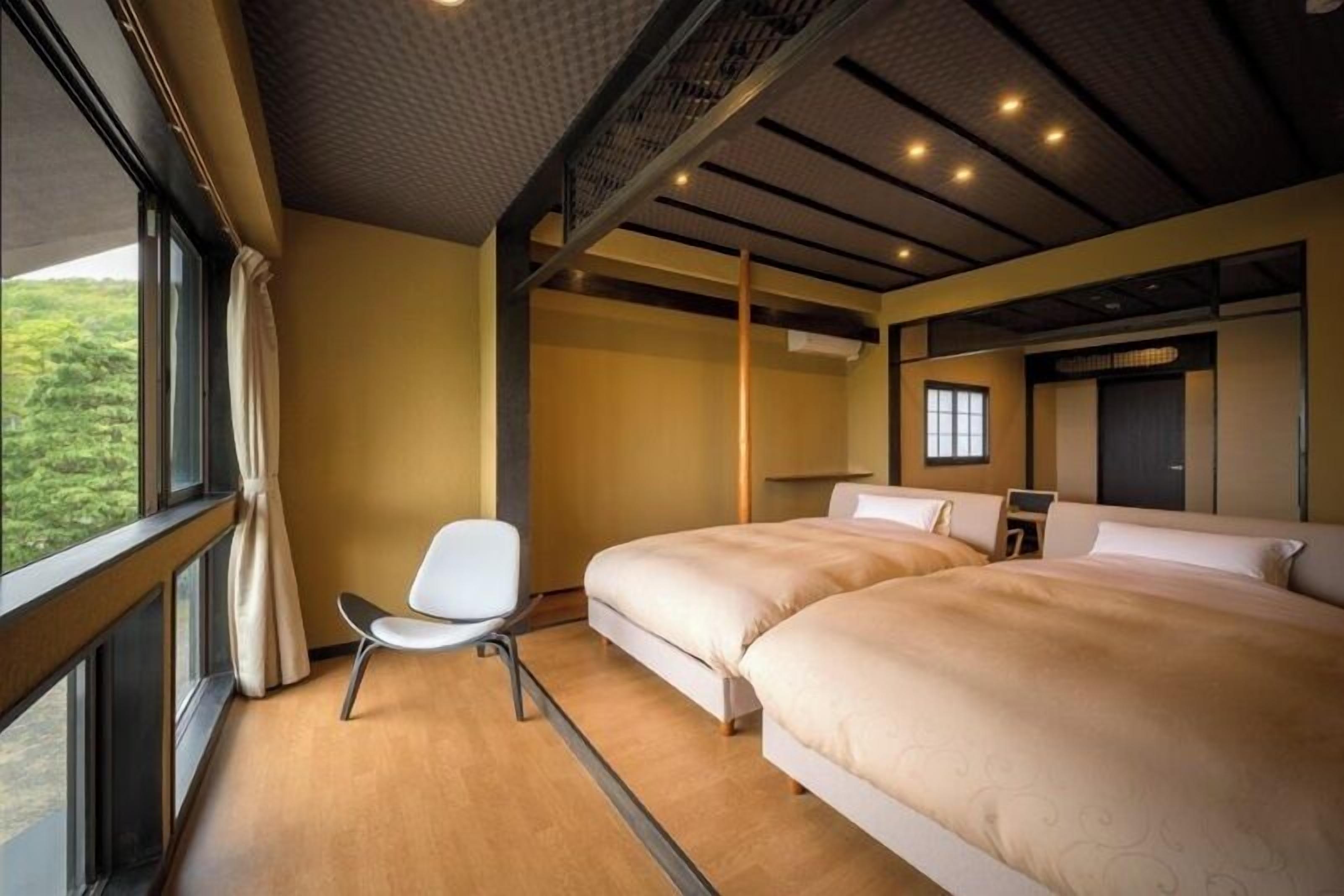 Une chambre d’hôtel avec deux lits, une chaise, une grande fenêtre et une vue sur la verdure.