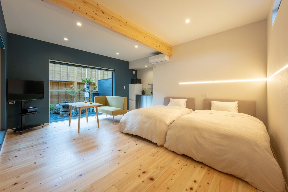 Een moderne slaapkamer met een groot bed, een televisie, een eettafel en uitzicht op een tuin.