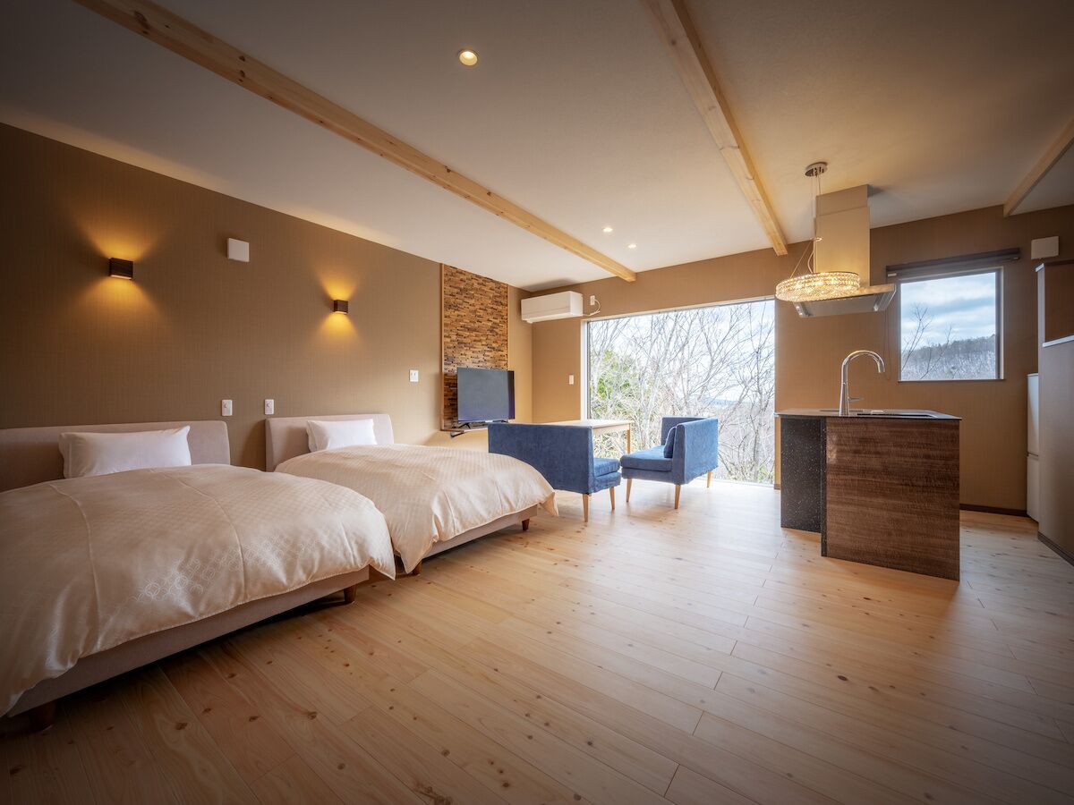 Une chambre moderne avec deux lits, un petit coin salon et un comptoir de cuisine.