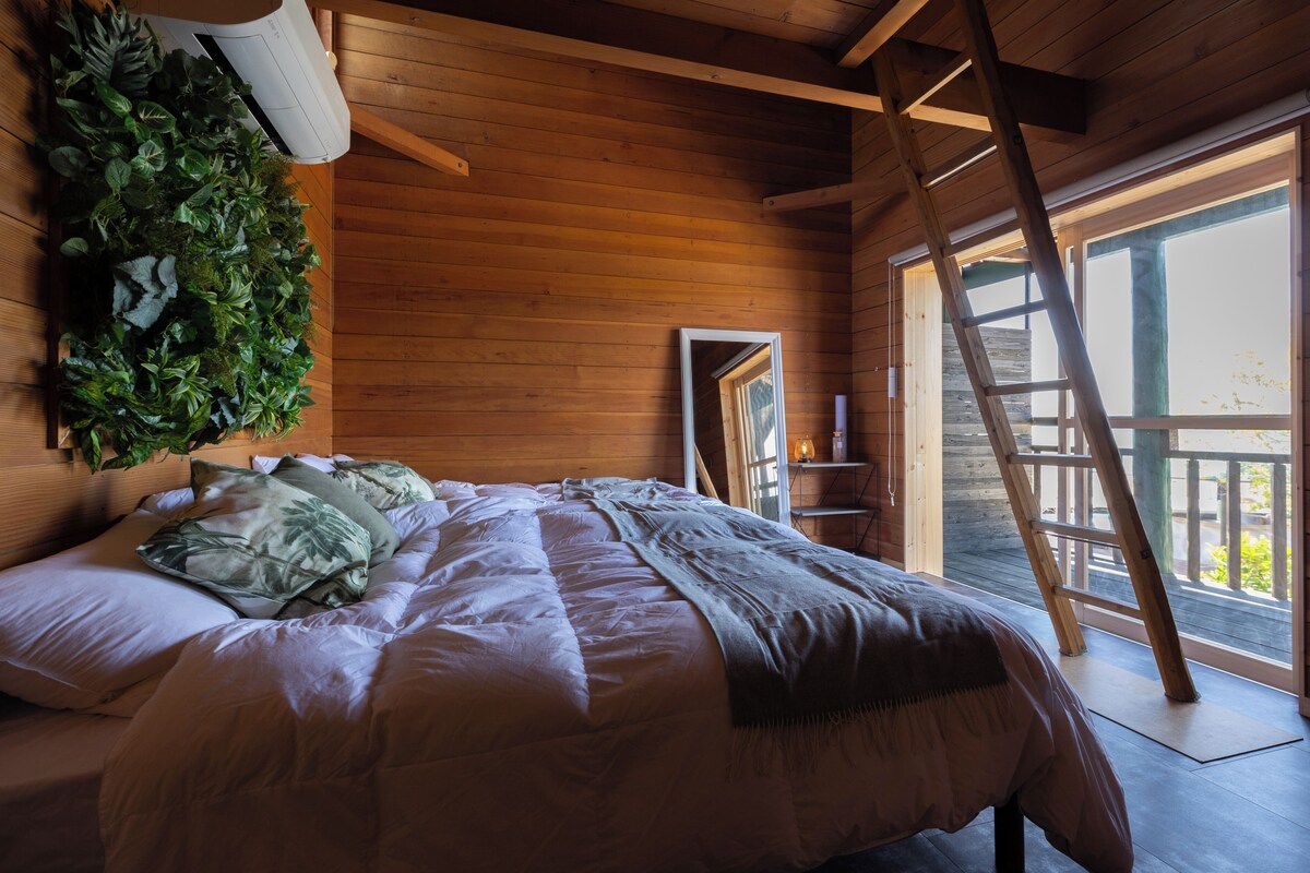 Camera da letto in una baita di legno, con un letto, una scala, una finestra e un condizionatore d'aria a parete.