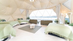 A spacious tented accommodation with a large bed, sofa, and a small table. - LIT Shimanami (Onomichi)