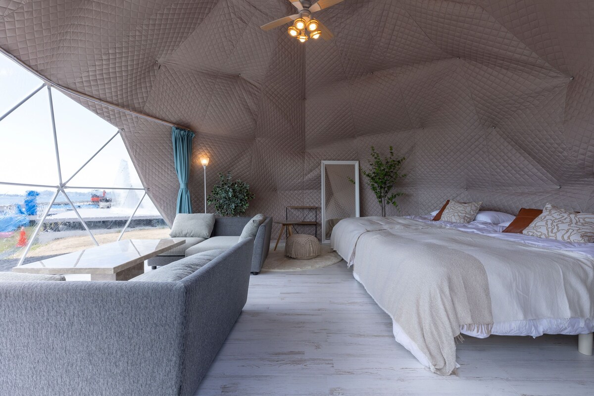 Una camera accogliente con un letto, un divano e un piccolo tavolo, caratterizzata da un soffitto dal design geometrico e ampie finestre.