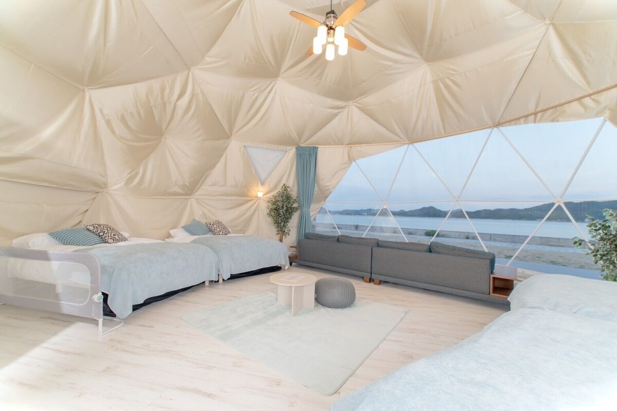 Un interno accogliente, simile a una tenda, con due letti, una ventola a soffitto e un'ampia finestra con vista sul mare.