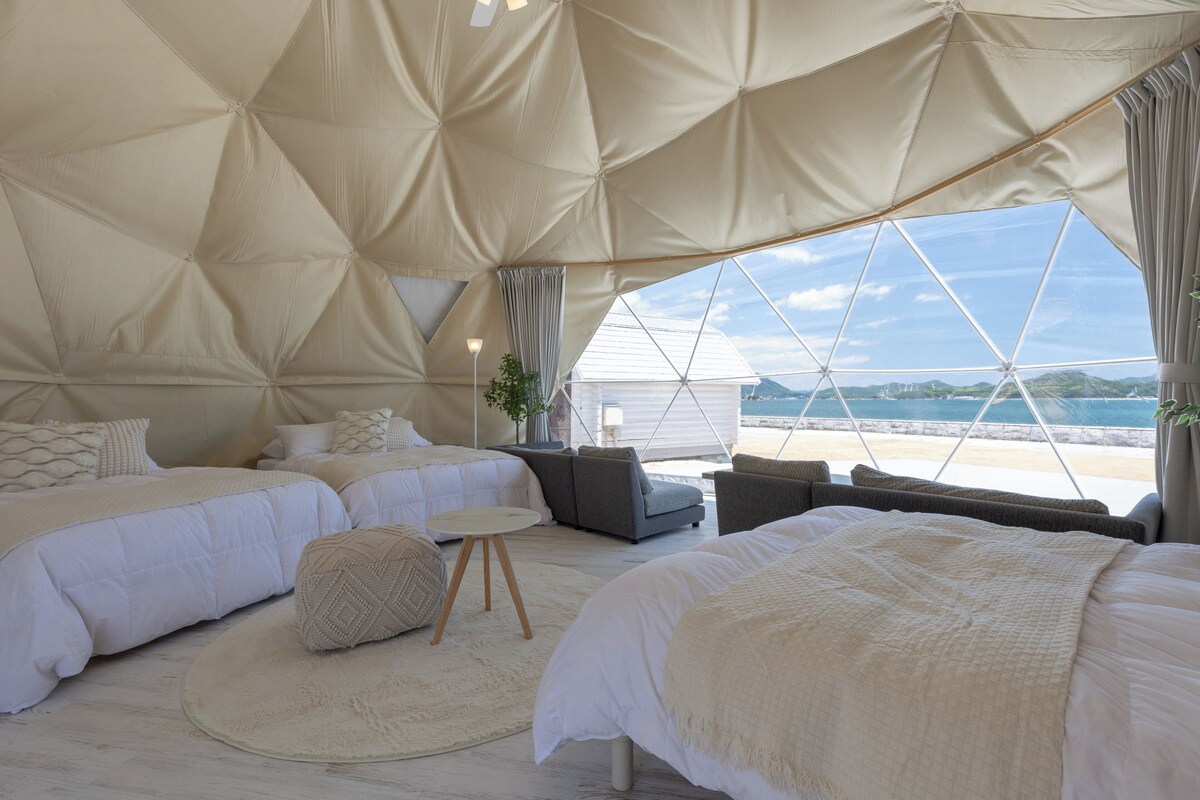 Un'accogliente sistemazione in tenda con due letti, un tavolo rotondo e vista sulla spiaggia.
