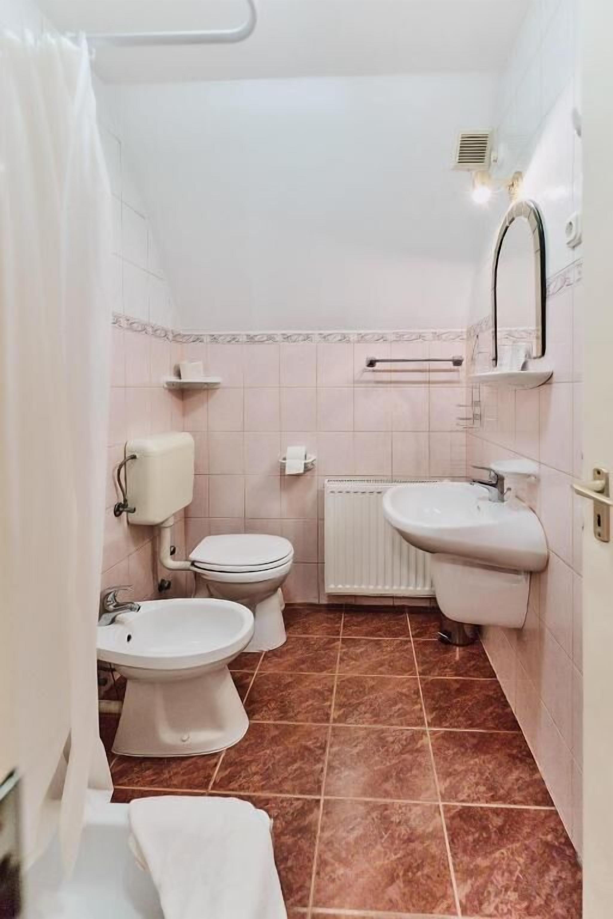 A bathroom with a toilet, bidet, and sink, tiled floor, and a radiator.