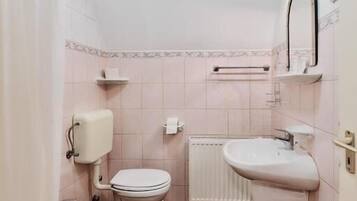 A bathroom with a toilet, bidet, and sink, tiled floor, and a radiator.