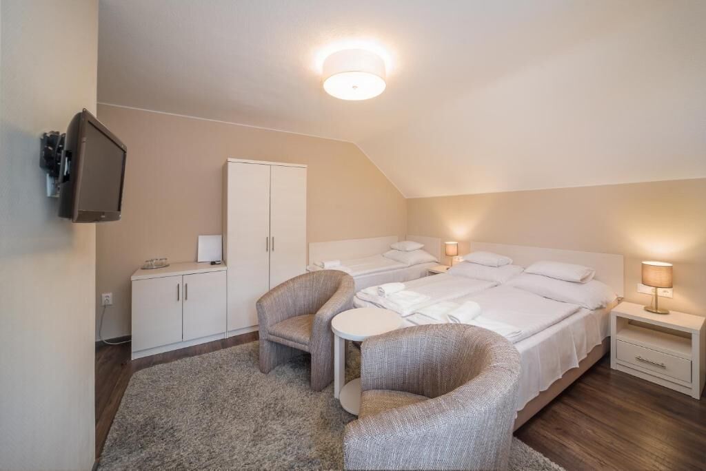 A room with two beds, a TV, a wardrobe, a small table, and two armchairs.