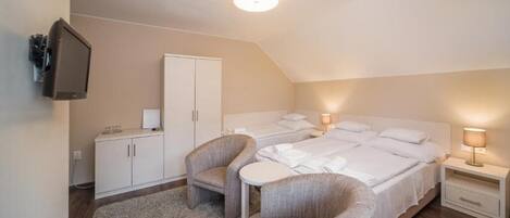 A room with two beds, a TV, a wardrobe, a small table, and two armchairs.