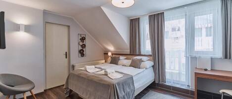 A bedroom with a bed, a desk, a chair, a door, and a window.