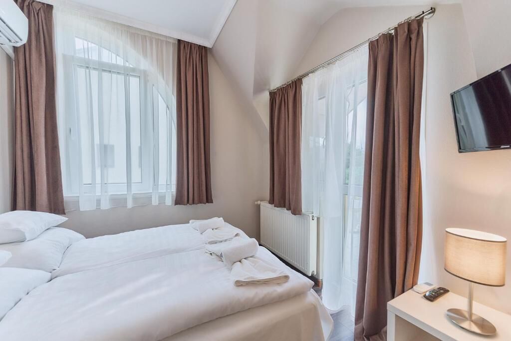Una camera d'albergo con due letti, una TV, una lampada e una finestra con tende.
