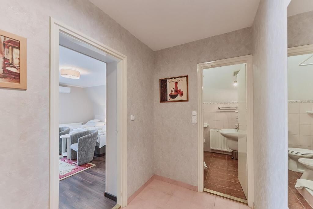 A hallway leading to a bedroom with a bed and a dining area, a bathroom with a toilet and sink, and a framed picture on the wall.