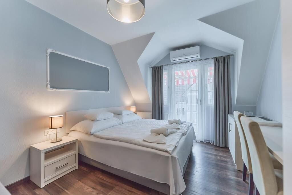 A modern bedroom with a large bed, bedside tables, a desk, and an air conditioning unit.