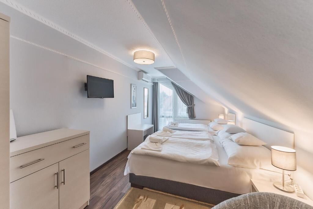 A modern hotel room with a large bed, bedside tables, a flat-screen TV, and a window with curtains.