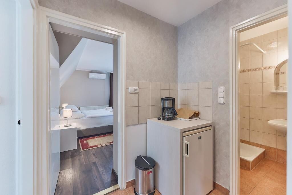 Una camera d'albergo compatta con angolo cottura, un piccolo cestino e un bagno con lavandino e doccia.