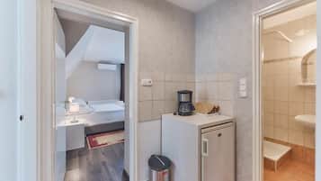 Una camera d'albergo compatta con angolo cottura, un piccolo cestino e un bagno con lavandino e doccia.