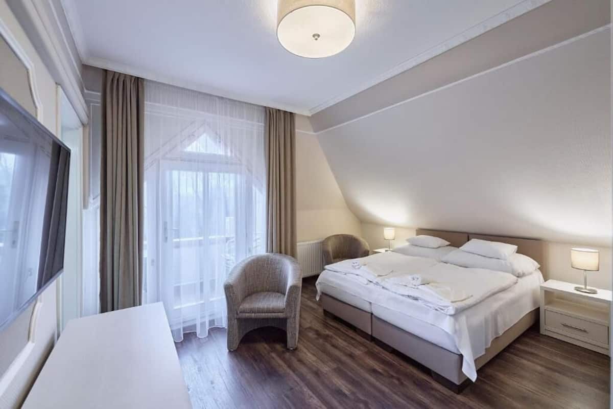 Une chambre d’hôtel avec un lit, une chaise, une table de chevet et une grande fenêtre avec des rideaux.