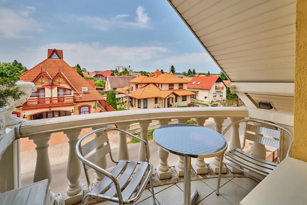 A balcony with a table and chairs, overlooking a residential area with red-roofed houses.